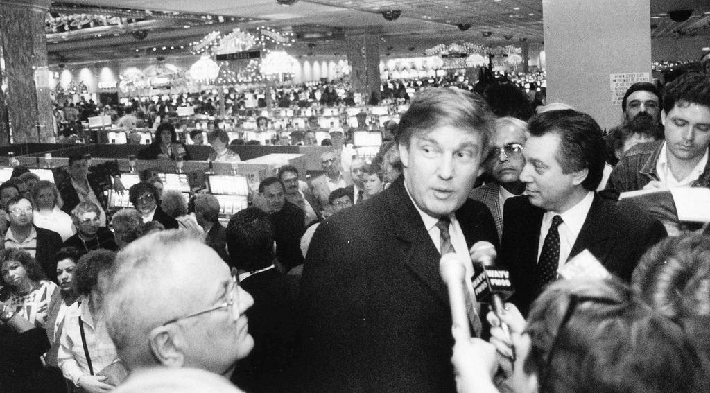 NYC-Walks-Blog-82a-Doanld-Trump-talks-to-the-press-on-the-opening-day-of-the-Trump-Taj-Mahal-Casino-Resort-9-April-1990-28275067675_a0d2dc87c9_b Donald Trump et al. sitting in front of a crowd